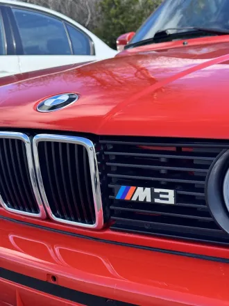 Gros plan sur la calandre et le badge M3 de la BMW M3 E30 rouge.