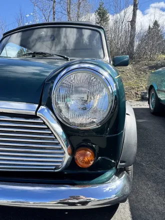 Gros plan sur le phare rond et la calandre chromée de la MINI classique vert foncé.